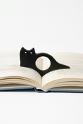 Black cat-shaped page holder on an open book against a white background