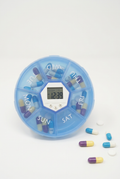 Blue seven-day pill box with central reminder clock and pills on a white background