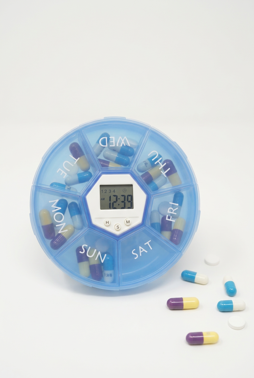 Blue seven-day pill box with central reminder clock and pills on a white background